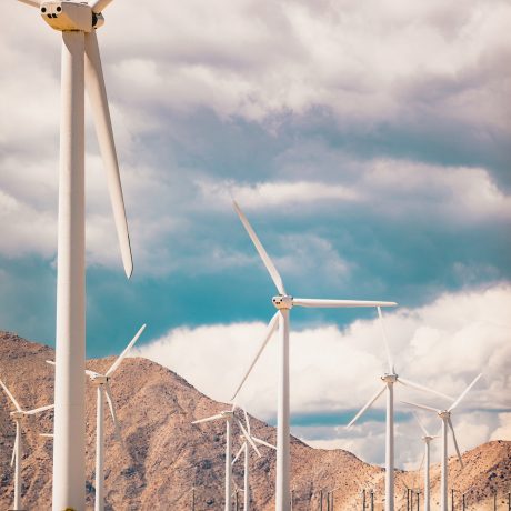 A vertical low angle shot of a lot of windmills in a field surrounded by high rocky mountains